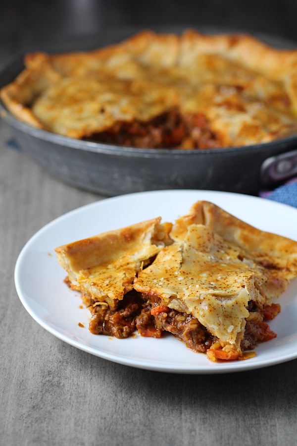 Piece of Flaky Empanada Pie with Ground Beef on a plate with skillet in background