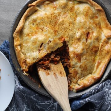 Savory Empanada Beef Pie Recipe in a skillet with spatula and piece out on counter. It has a perfect flaky, buttery pastry on the outside with a savory, smokey, salty ground beef filling. The best part is that everything cooks in one skillet!