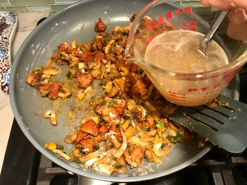 Adding broth to pan with chorizo, mushrooms, flour for Creamy Green Beans and Mushrooms with Chorizo in a serving bowl are a creamy and savory side dish.