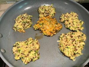 Lentil and Zucchini Cakes starting to cook in a frying pan with center cake flipped over. They have a crispy outside and soft inside and are perfect for an easy dinner! The flavors are simple but perfect with parmesan, oregano, scallions, lentils, and zucchini.