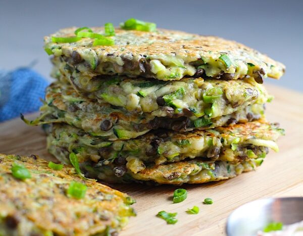 Lentil and Zucchini Cakes stacked on wood cutting board. They have a crispy outside and soft inside and are perfect for an easy dinner! The flavors are simple but perfect with parmesan, oregano, scallions, lentils, and zucchini.