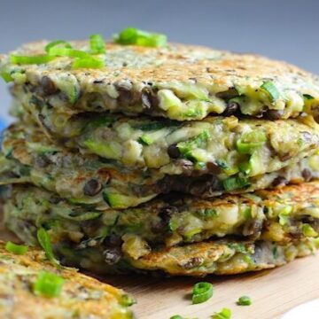 Lentil and Zucchini Cakes stacked on wood cutting board. They have a crispy outside and soft inside and are perfect for an easy dinner! The flavors are simple but perfect with parmesan, oregano, scallions, lentils, and zucchini.