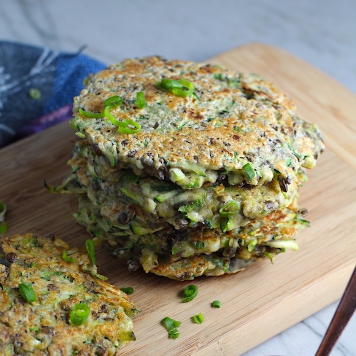 Zucchini Lentil Fritters stacked on wood cutting board. They have a crispy outside and soft inside and are perfect for an easy dinner! The flavors are simple but perfect with parmesan, oregano, scallions, lentils, and zucchini.