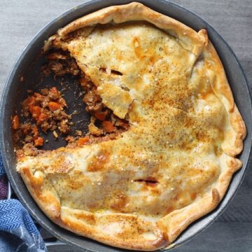 Flaky Empanada Pie with Ground Beef Recipe in a skillet with a piece out on counter. It has a perfect flaky, buttery pastry on the outside with a savory, smokey, salty ground beef filling. The best part is that everything cooks in one skillet!