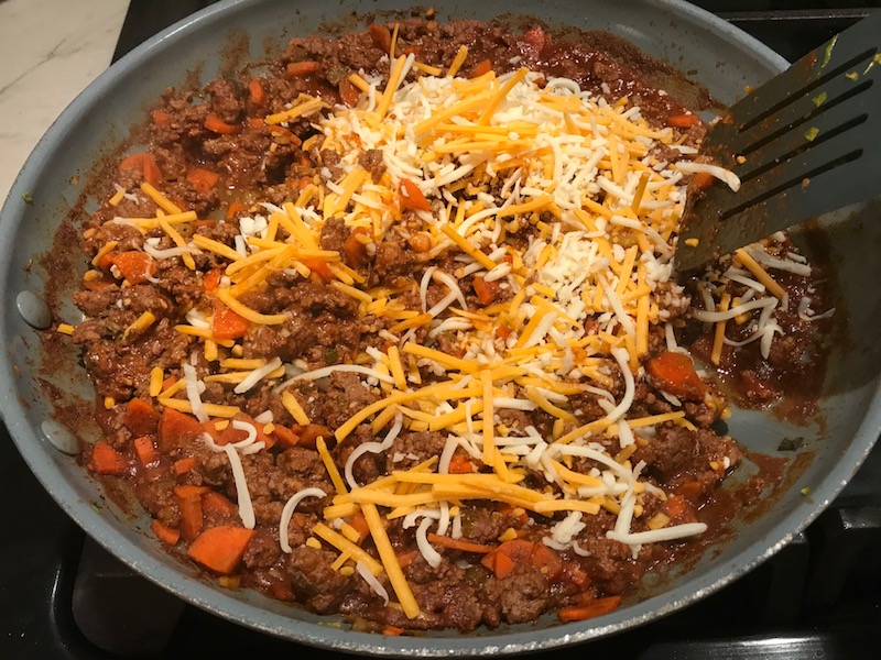 Shredded cheese on top of beef mixture in skillet for Empanada Beef Pie Recipe. It has a perfect flaky, buttery pastry on the outside with a savory, smokey, salty ground beef filling. The best part is that everything cooks in one skillet!
