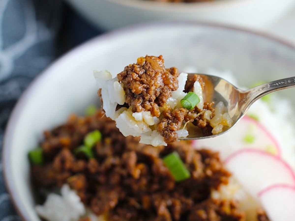 Spoon with bite of Korean Bulgogi Ground Beef and Rice with bowl below with sliced radishes fanned out on top and scallion garnish.