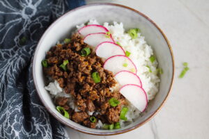 Korean Ground Beef and Rice Bowl with sliced radishes fanned out on top and scallion garnish.