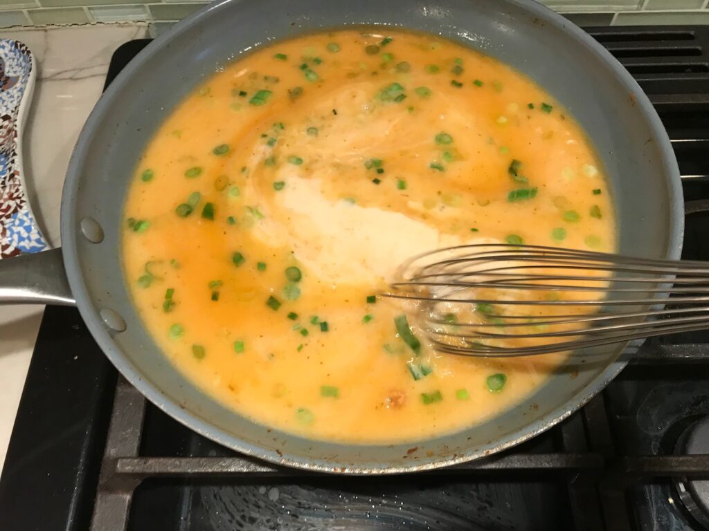 Whisk mixing sauce with scallions in a frying pan for Quick Cooking Creamy Chicken Paprika. It's creamy, smokey, rich, and hearty. This is an easy weeknight family dinner!