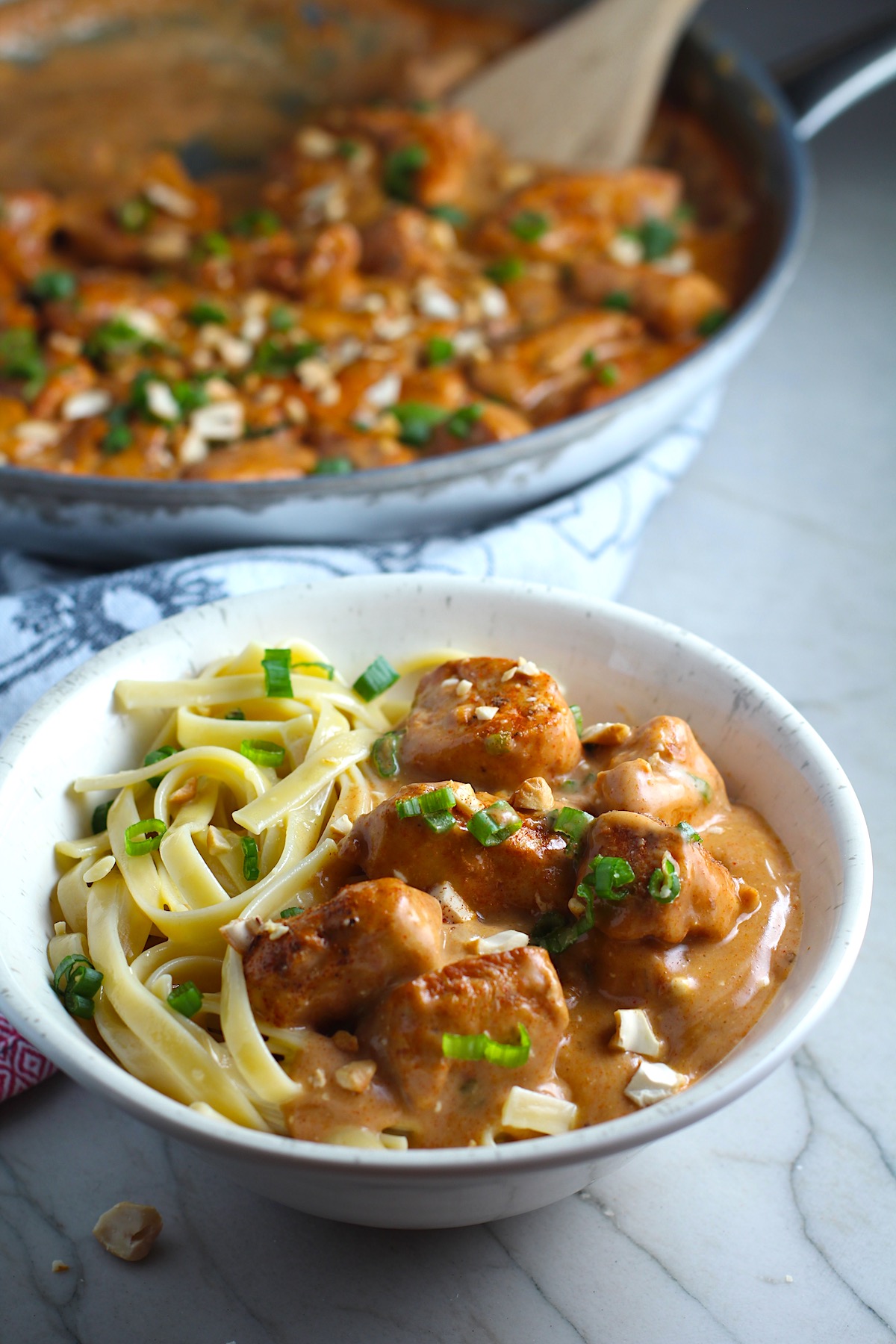 Quick Cooking Creamy Paprika Chicken in a bowl with pasta and pan in background. It's creamy, smokey, rich, and hearty. This is an easy weeknight family dinner!