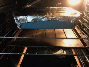 Greek Ground Chicken Feta Pasta Casserole in oven with aluminum foil on top. It has lean ground chicken with garlic, oregano, parmesan, feta and Kale.