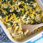 Greek Ground Chicken Feta Pasta Casserole in a casserole dish with wood spatula. It has lean ground chicken with garlic, oregano, parmesan, feta and Kale. 