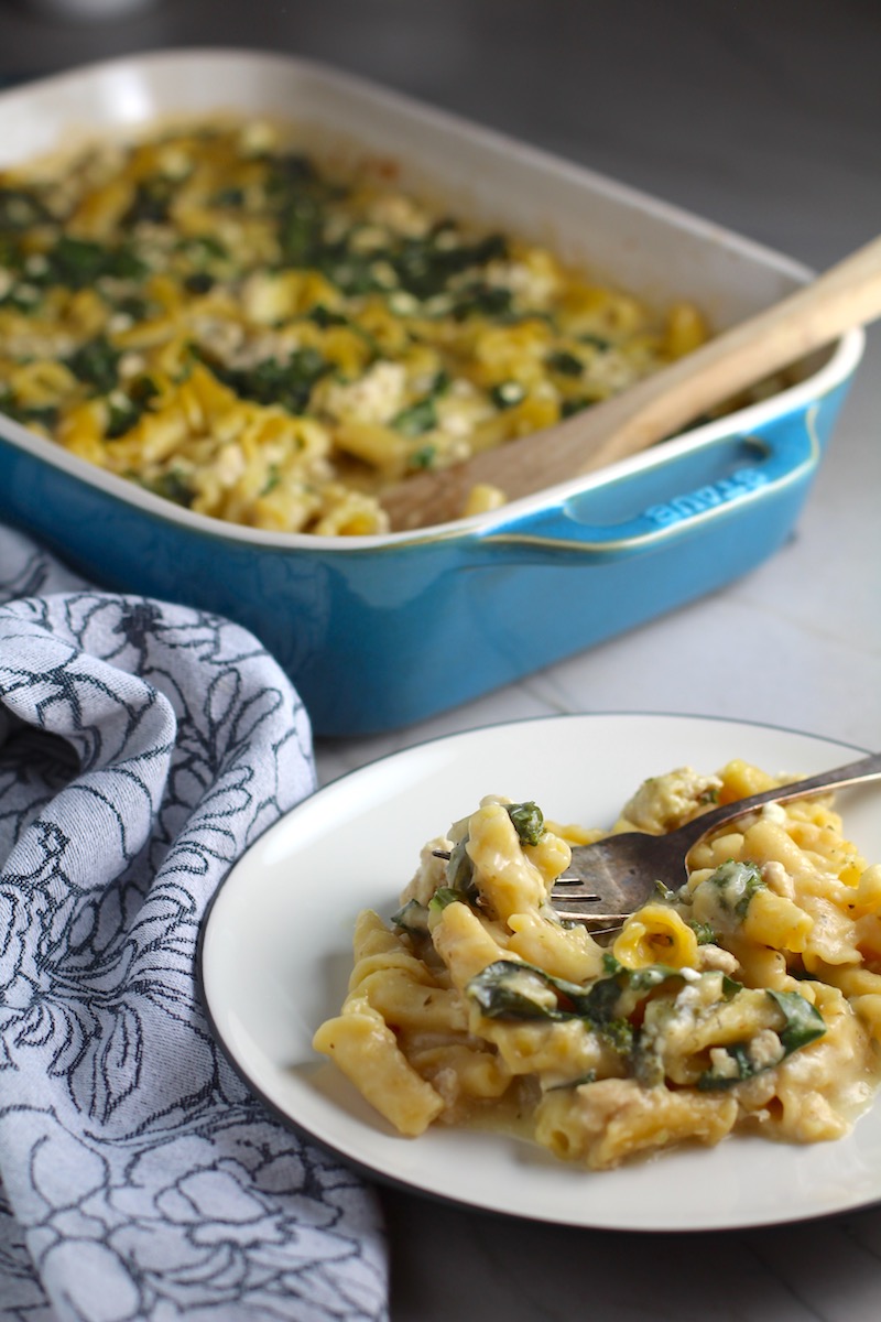 Greek Ground Chicken Feta Pasta Casserole on a plate with fork and casserole in background. It has lean ground chicken with garlic, oregano, parmesan, feta and Kale.