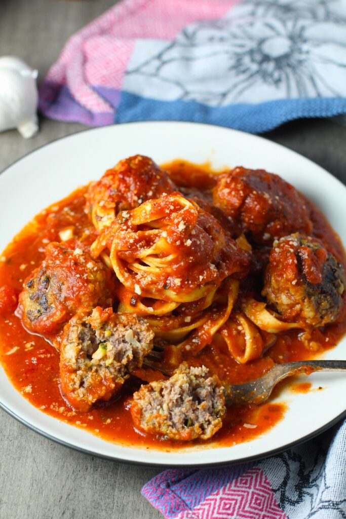 Healthy Meatballs with Zucchini & Lean Beef on a plate with tomato sauce and fettuccine in the center. They're loaded with flavor from the garlic, minced onion, salt, and pepper. The zucchini brings moisture, texture, and bulks up the meatballs with healthiness.