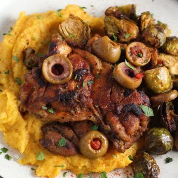 Sheet Pan Spanish Chicken thighs on a plate with Butternut Squash Mash, Olives, and Brussels Sprouts! It's warm, hearty, and smoky.