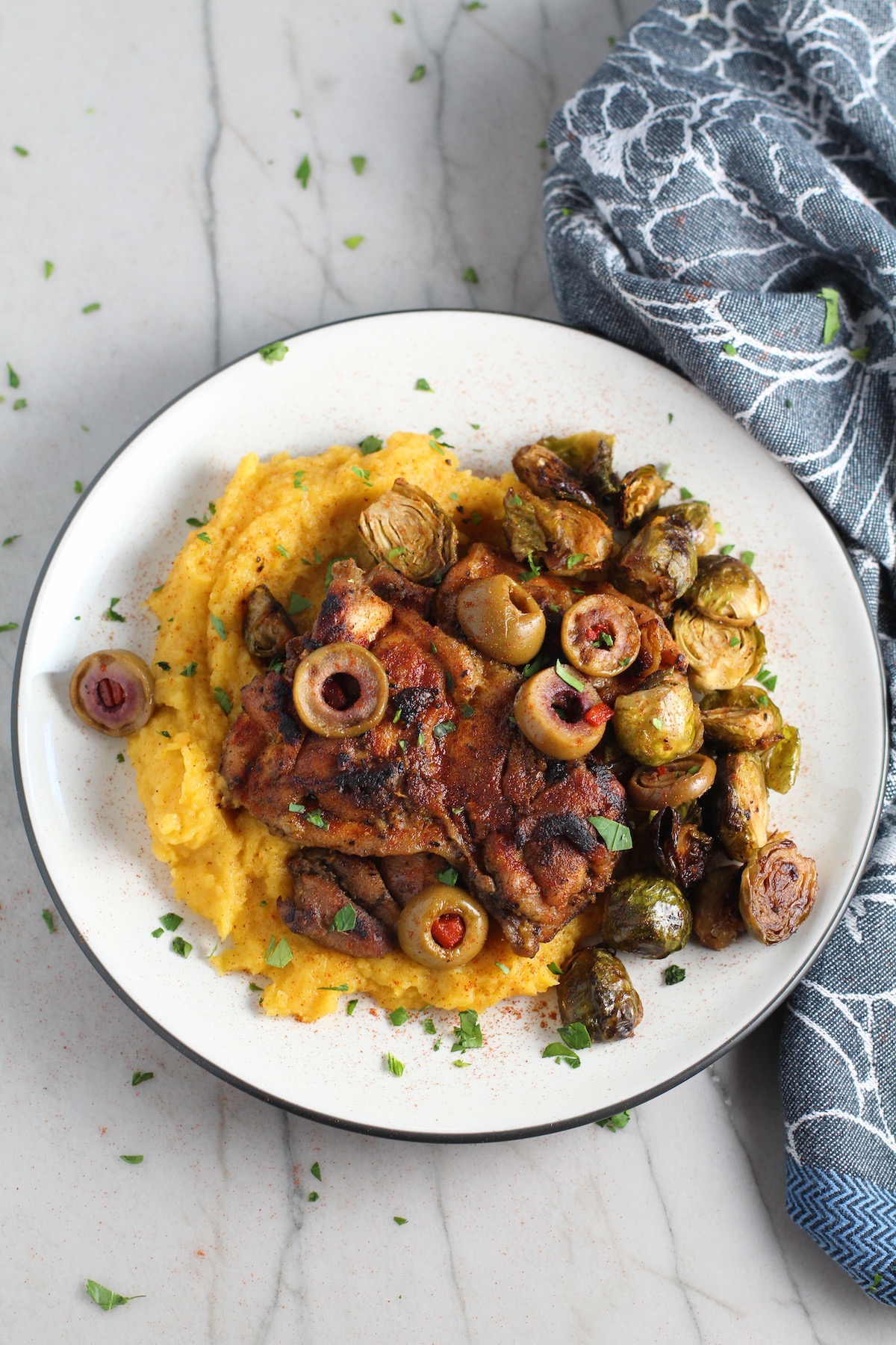Sheet Pan Spanish Chicken thighs on a plate with Butternut Squash Mash, Olives, and Brussels Sprouts! It's warm, hearty, and smoky.