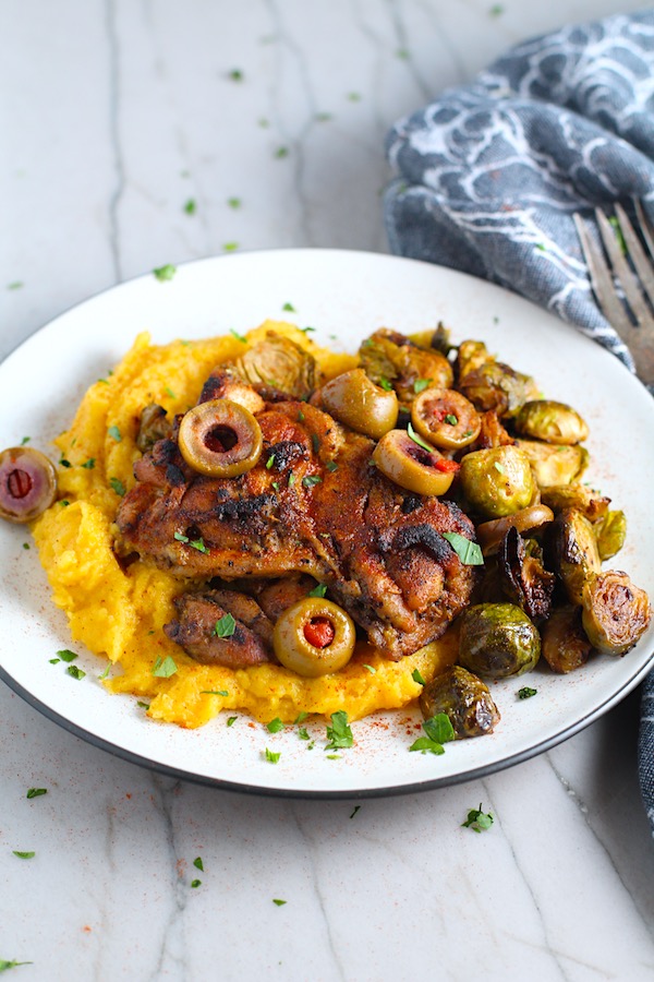 Sheet Pan Spanish Chicken thighs on a plate with Butternut Squash Mash, Olives, and Brussels Sprouts! It's warm, hearty, and smoky.