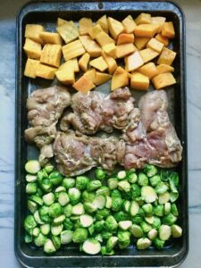 Sheet Pan Spanish Chicken thighs on a pan with Butternut Squash cubes in one side and Brussels Sprouts on the other! It's warm, hearty, and smoky.