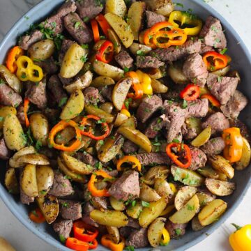 Garlic Potato and Steak Bites Recipe with sweet pepper slices in a pan on counter. It's an easy and delicious, one-pan family dinner! You get fantastic salty, buttery, tender steak and potatoes in each and every mouthwatering bite!