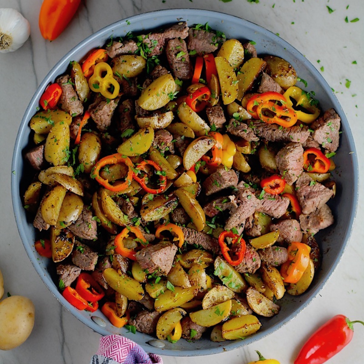 Garlic Potato and Steak Bites Recipe with sweet pepper slices in a pan on counter. It's an easy and delicious, one-pan family dinner!  You get fantastic salty, buttery, tender steak and potatoes in each and every mouthwatering bite! 