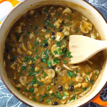 Creamy Cajun Cauliflower and Beans in a pot with wood spoon. The mild cajun flavors combined with  healthy garbanzo beans, black beans, cauliflower, and mushrooms make this a hearty, creamy, and delicious dish