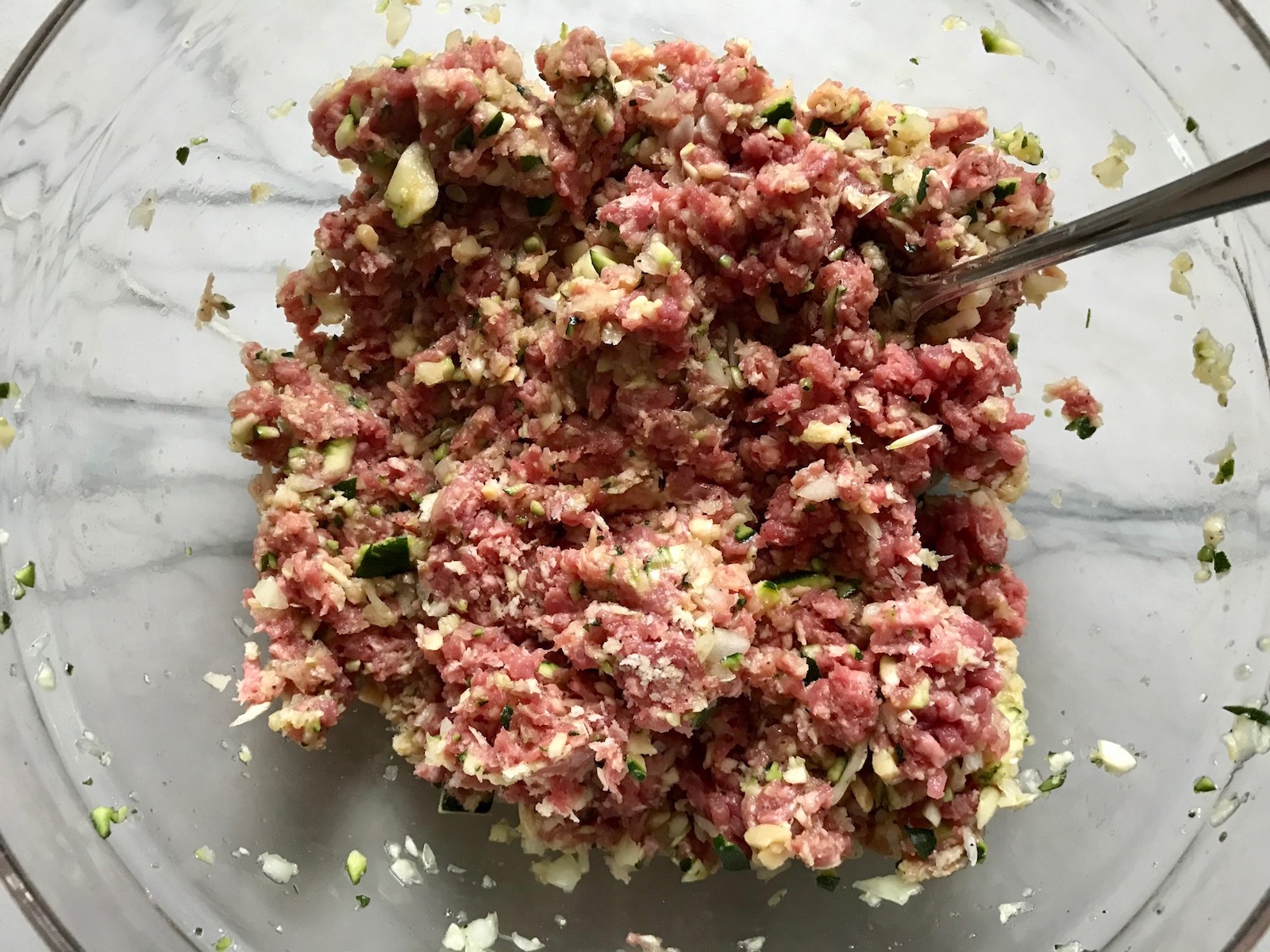 Meatball ingredients mixed in bowl for Healthy Meatballs with Zucchini & Lean Beef. They're loaded with flavor from the garlic, minced onion, salt, and pepper. The zucchini brings moisture, texture, and bulks up the meatballs with healthiness.