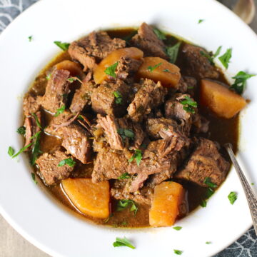 Slow Cooker Honey Garlic Beef and Potatoes in a bowl with parsley on top. It's a delicious easy dinner with tender beef cubes are cooked in the slow cooker with lots of delicious garlic, onions, and potatoes. Then honey and molasses are added for that touch of sweet.