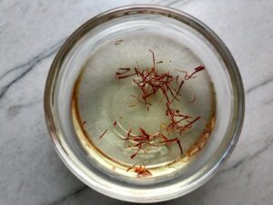 Saffron blooming in water in a bowl for Saffron Butter Crispy Rice. Saffron brings a floral note and beautiful yellow-orange color. Added to the butter is what gives this crispy rice the buttery, crispy bottom.