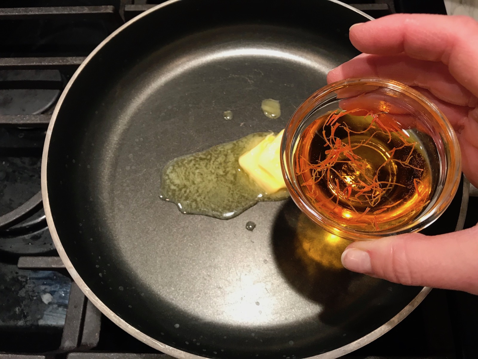 Hand about to pour saffron into pan with melted butter for Saffron Butter Crispy Rice. Saffron brings a floral note and beautiful yellow-orange color. Added to the butter is what gives this crispy rice the buttery, crispy bottom.