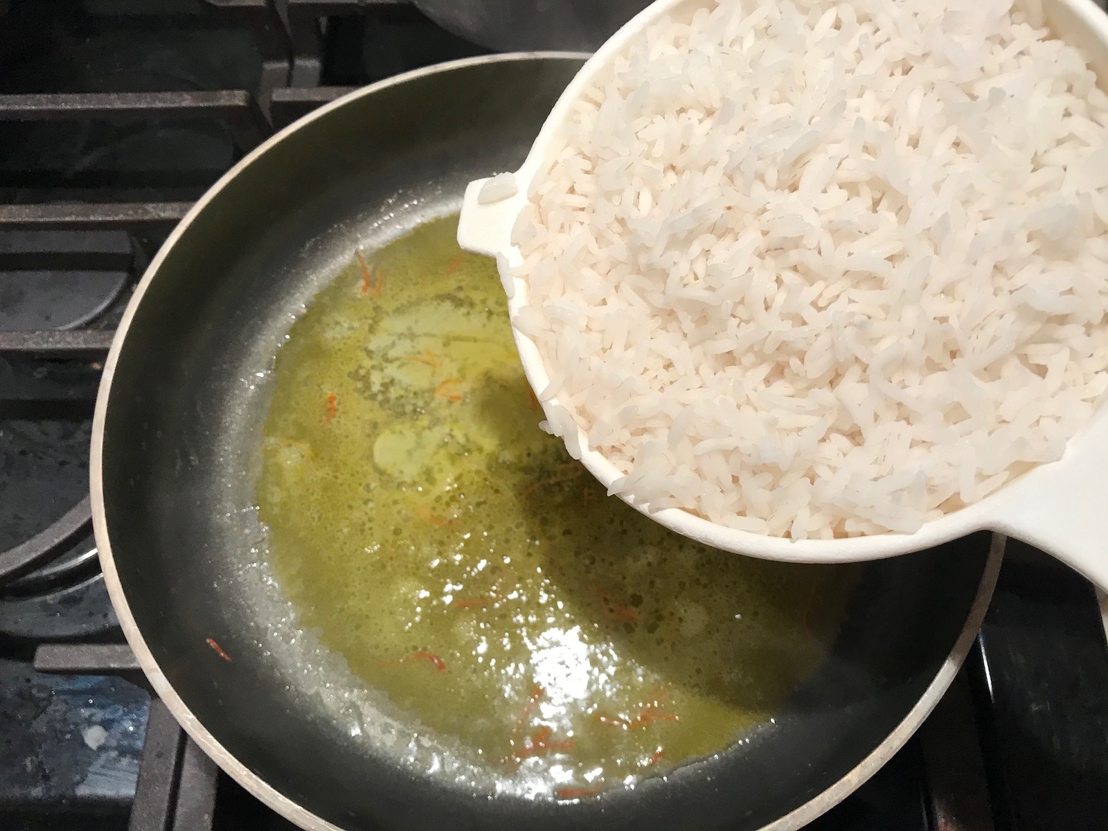Pouring cooked rice from strainer to pan with melted butter and saffron for Saffron Butter Crispy Rice. Saffron brings a floral note and beautiful yellow-orange color. Added to the butter is what gives this crispy rice the buttery, crispy bottom.