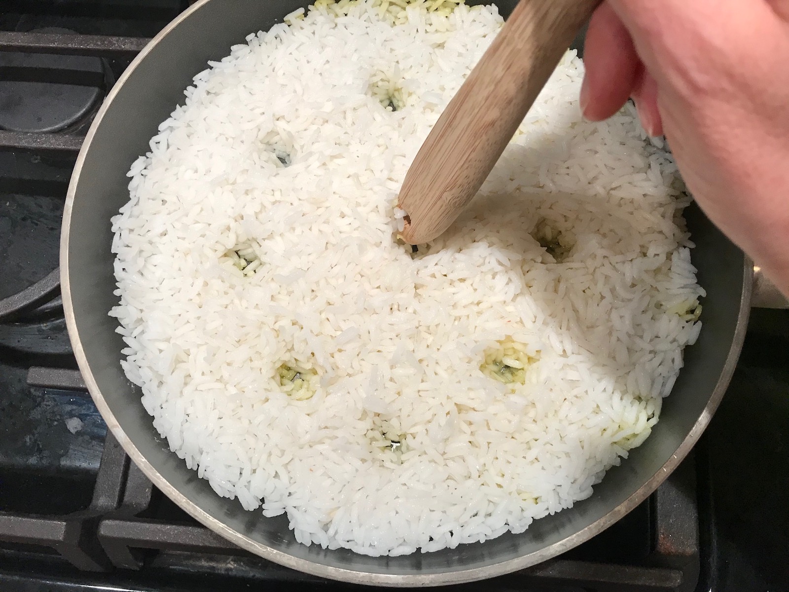 Spoon handle poking holes into cooked rice in pan for Saffron Butter Crispy Rice. Saffron brings a floral note and beautiful yellow-orange color. Added to the butter is what gives this crispy rice the buttery, crispy bottom.