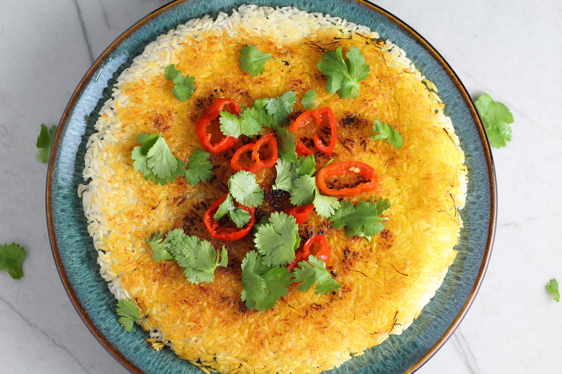 Saffron Butter Crispy Rice on a plate with cilantro and peppadew peppers on top. Saffron brings a floral note and beautiful yellow-orange color. Added to the butter is what gives this crispy rice the buttery, crispy bottom.