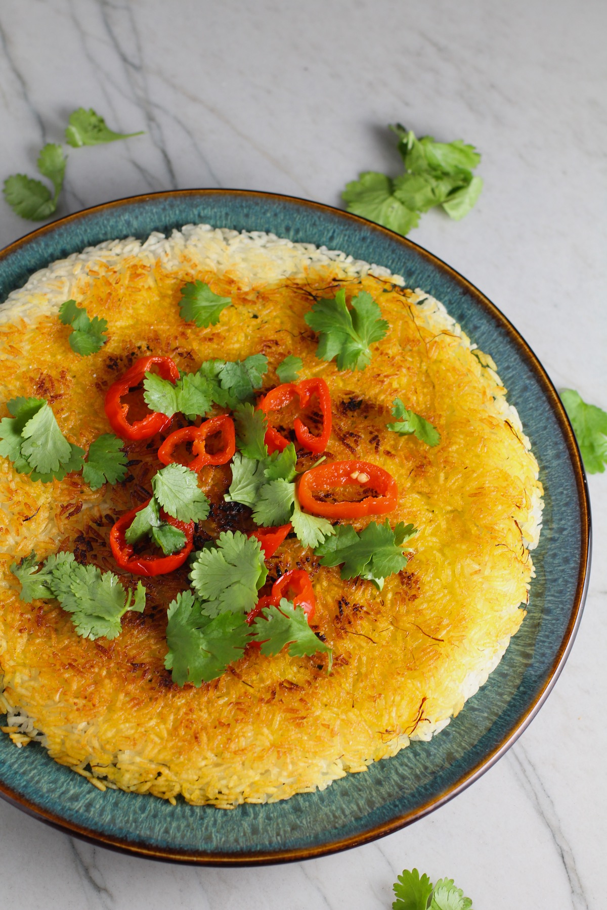 Saffron Butter Crispy Rice on a plate with cilantro and peppadew peppers on top. Saffron brings a floral note and beautiful yellow-orange color. Added to the butter is what gives this crispy rice the buttery, crispy bottom.