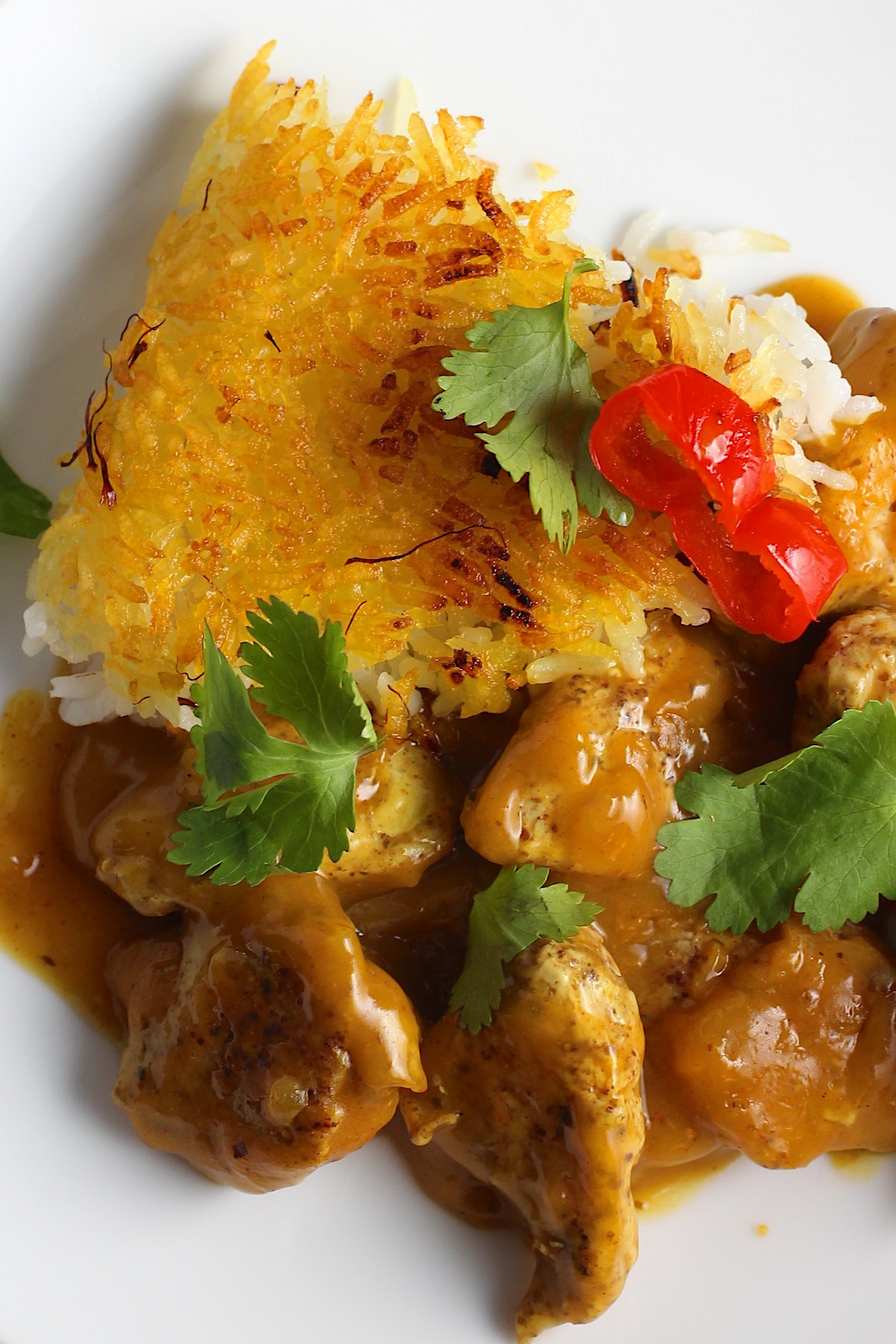 Saffron Butter Crispy Rice slice on a plate with chicken and cilantro and peppadew peppers on top. Saffron brings a floral note and beautiful yellow-orange color. Added to the butter is what gives this crispy rice the buttery, crispy bottom.
