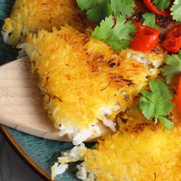 Saffron Butter Crispy Rice on a plate with cilantro and peppadew peppers on top. Spatula scooping up a triangle piece. Saffron brings a floral note and beautiful yellow-orange color. Added to the butter is what gives this crispy rice the buttery, crispy bottom.