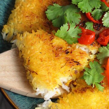 Saffron Butter Crispy Rice on a plate with cilantro and peppadew peppers on top. Spatula scooping up a triangle piece. Saffron brings a floral note and beautiful yellow-orange color.  Added to the butter is what gives this crispy rice the buttery, crispy bottom.