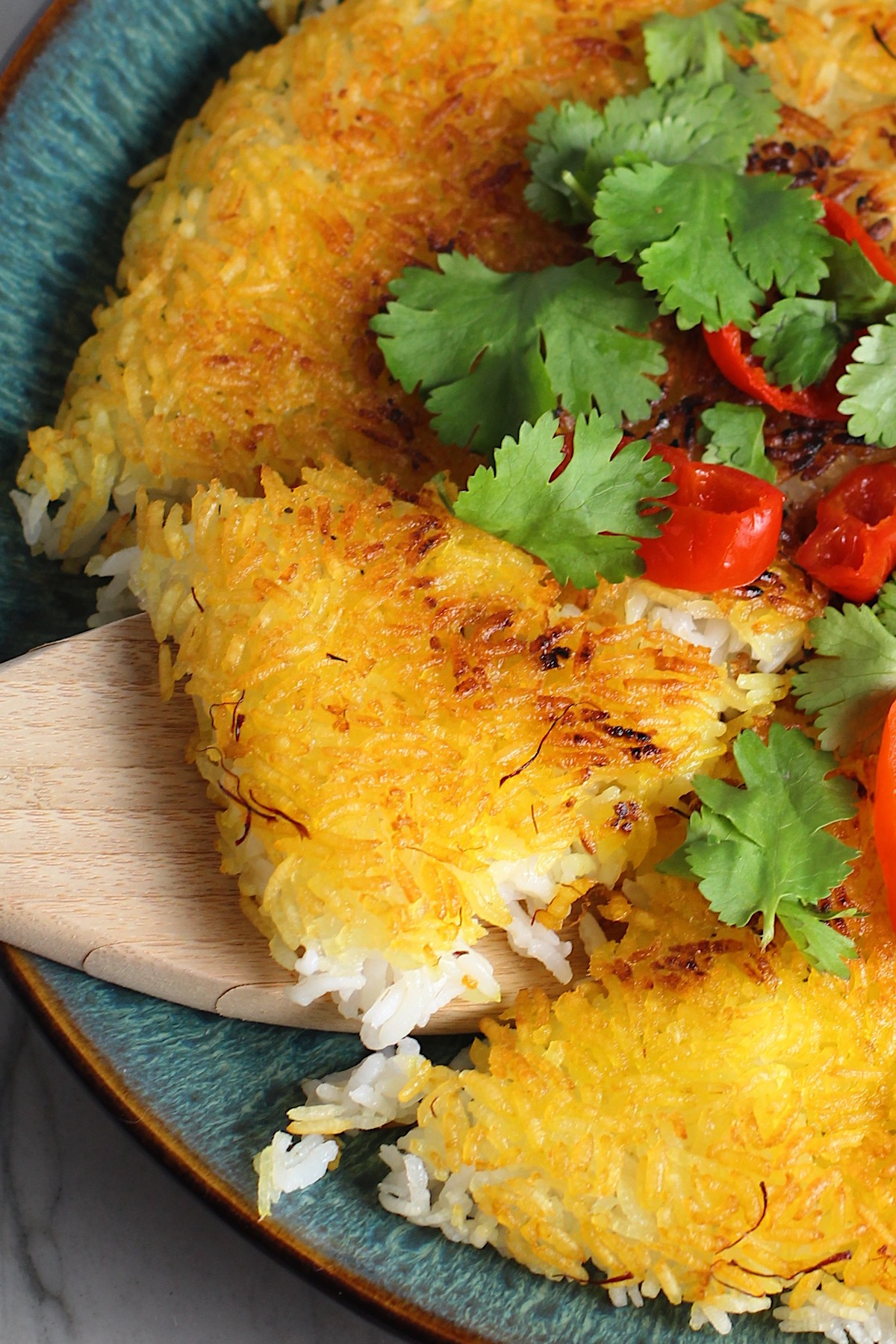 Saffron Butter Crispy Rice on a plate with cilantro and peppadew peppers on top. Spatula scooping up a triangle piece. Saffron brings a floral note and beautiful yellow-orange color. Added to the butter is what gives this crispy rice the buttery, crispy bottom.