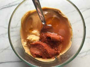 Peanut butter, thai curry paste, garlic, and honey in a bowl for Thai Peanut Sauce Noodles with seared tofu and veggies.