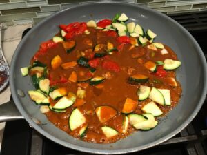 Thai peanut sauce added to zucchini and red pepper in a pan for Thai Peanut Sauce Noodles with seared tofu and veggies.