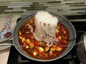 Cooked Rice noodles being added to a pan with Thai Peanut Sauce with tofu and veggies.