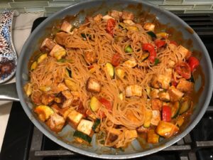 Thai Peanut Sauce Noodles with seared tofu and veggies in a pan on stove.