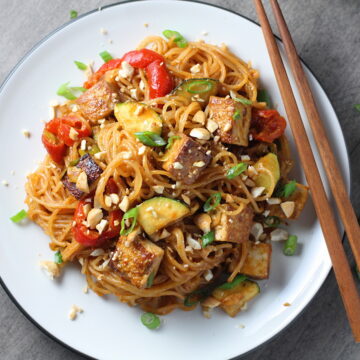 Thai Peanut Sauce Noodles with seared tofu and veggies on a plate with chopsticks.