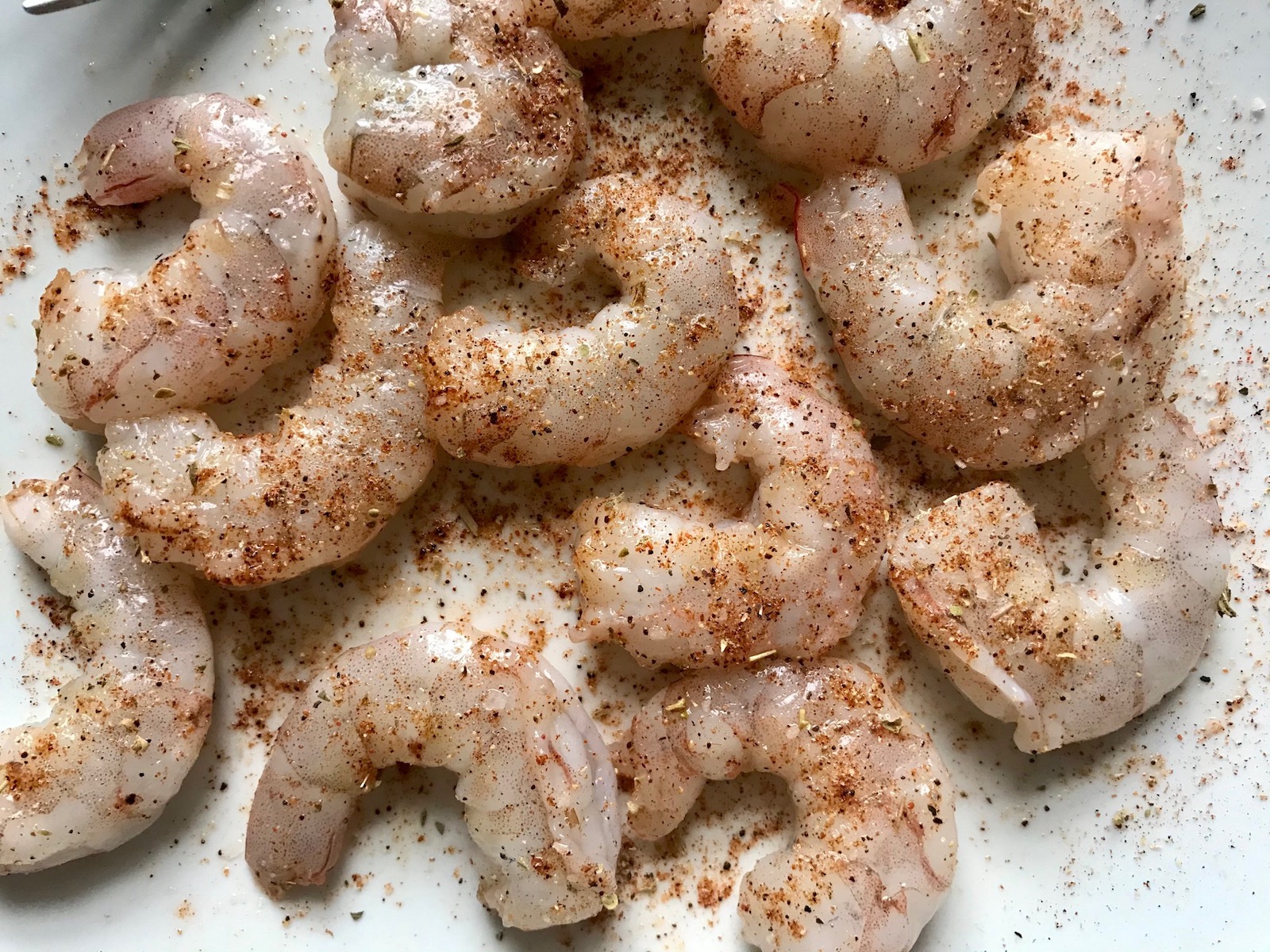 Cajun seasoning on raw shrimp without tails for Shrimp and Grits recipe.
