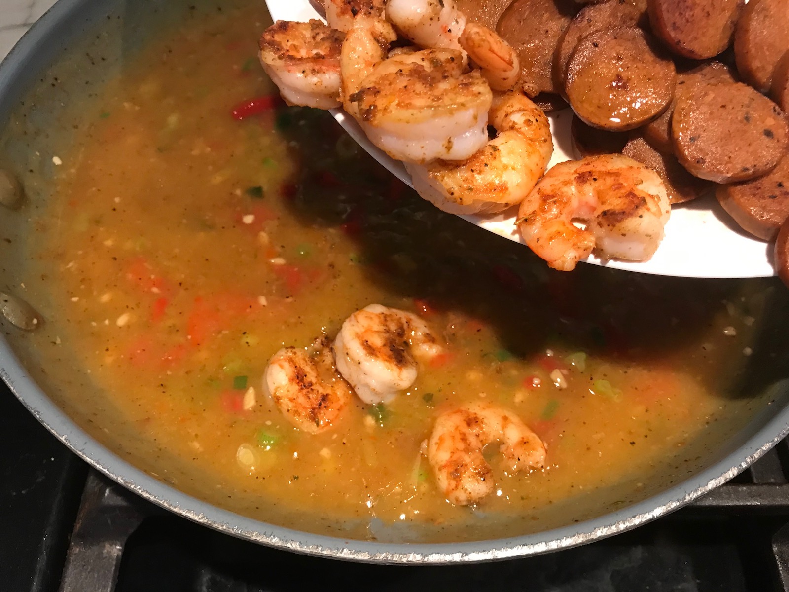 Adding cooked cajun shrimp and sausage back to sauce in a pan for Shrimp and Grits recipe.