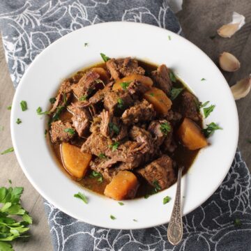 Slow Cooker Honey Garlic Beef and Potatoes in a bowl with parsley on top. It's a delicious easy dinner with tender beef cubes are cooked in the slow cooker with lots of delicious garlic, onions, and potatoes.  Then honey and molasses are added for that touch of sweet.