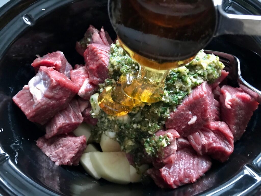 Pouring honey over raw beef and other ingredients in slow cooker for Honey Garlic Beef and Potatoes. It's a delicious easy dinner made in the slow cooker with tender beef cubes are cooked in the slow cooker with lots of delicious garlic, onions, and potatoes. Then honey and molasses are added for that touch of sweet.