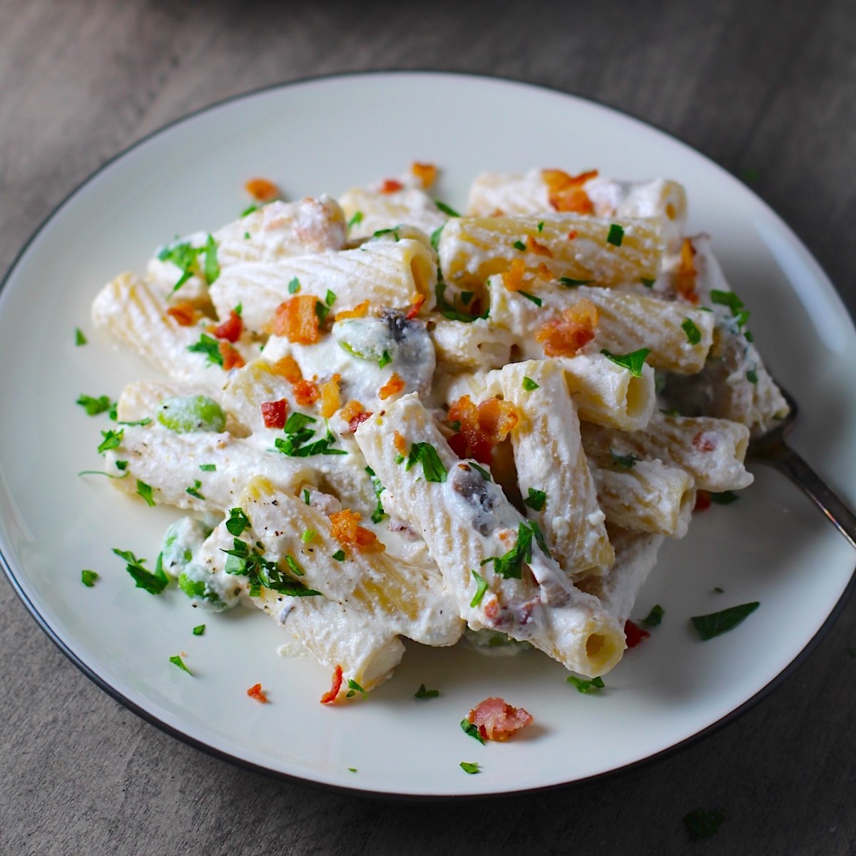 Pasta with Ricotta, Bacon, Mushroom Sauce on a plate with fork and pan in background. It's creamy, rich, decadent, comforting, and downright delicious! Finally, shelled edamame for a bit of color and texture!