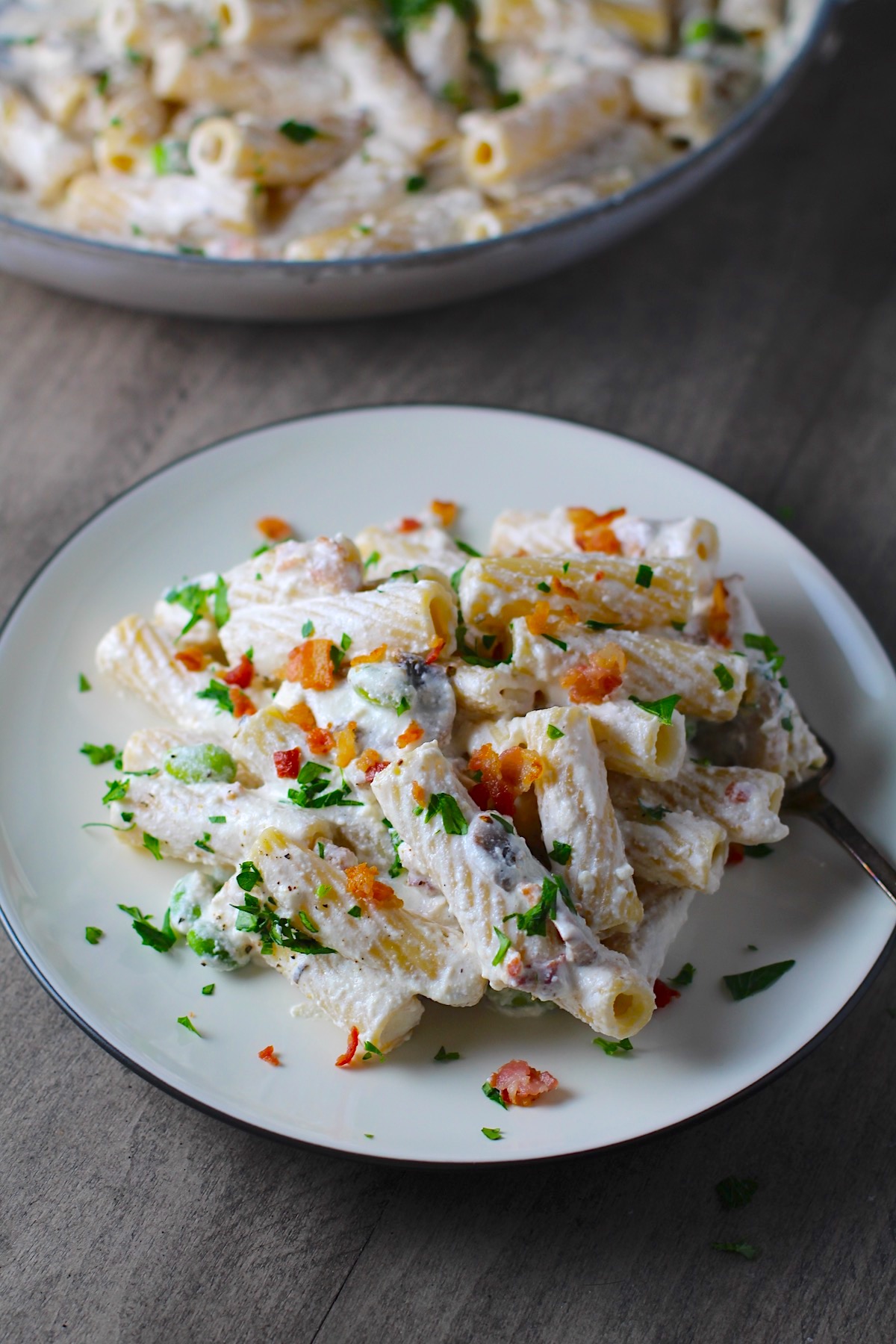 Pasta with Ricotta, Bacon, Mushroom Sauce on a plate with fork and pan in background. It's creamy, rich, decadent, comforting, and downright delicious! Finally, shelled edamame for a bit of color and texture!