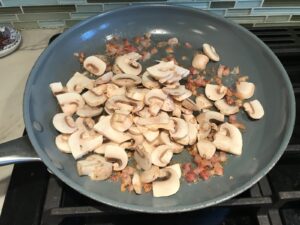 Mushroom slices and Bacon bits cooking in pan for Ricotta Sauce Pasta with Bacon and Mushrooms on stove. It's creamy, rich, decadent, comforting, and downright delicious!