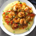 Cajun Shrimp and Grits recipe on a plate. It has seared shrimp in a creamy smoky cajun sauce with chicken andouille sausage and pimiento.  Served over creamy, cheesy grits.