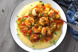Cajun Shrimp and Grits recipe on a plate. It has seared shrimp in a creamy smoky cajun sauce with chicken andouille sausage and pimiento. Served over creamy, cheesy grits.